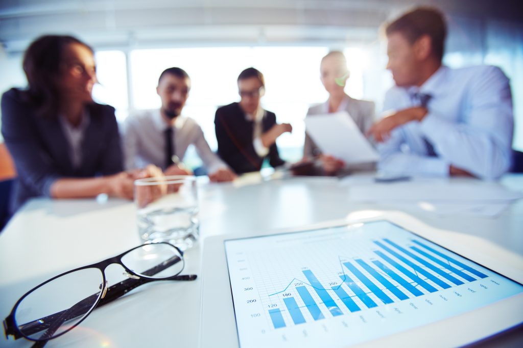 Blurry image of 4 office workers with tablet showing graph in the foreground