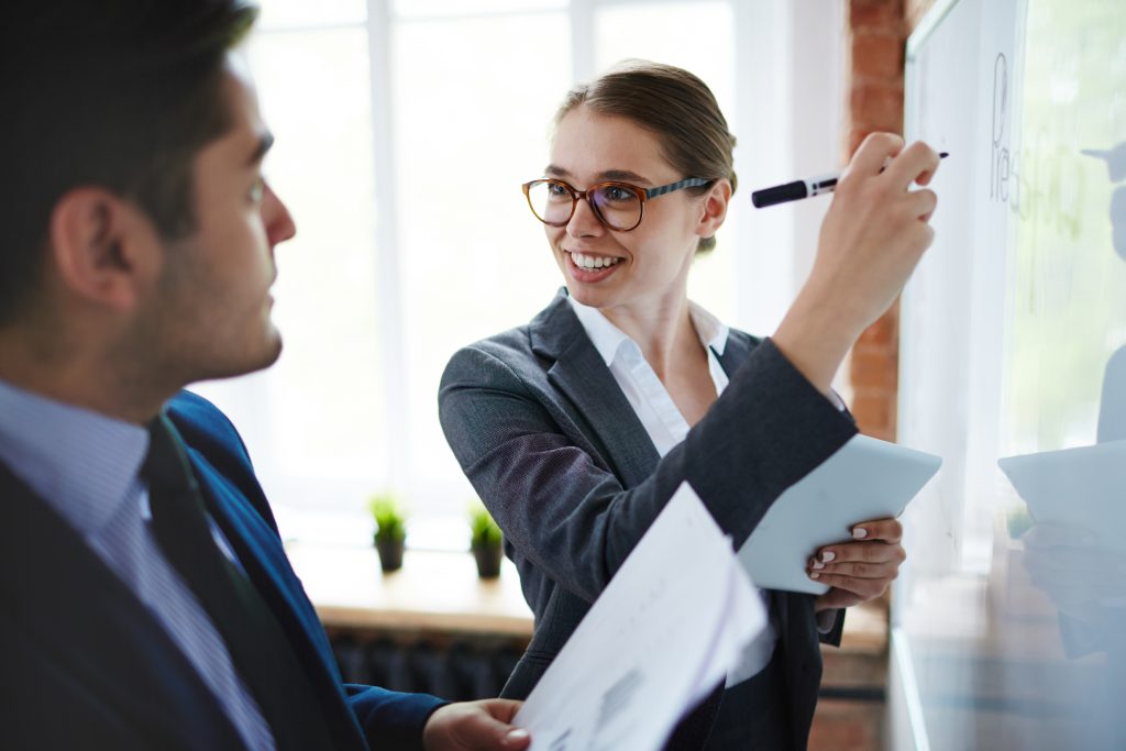 Female colleague writing on whiteboard showing insight to her male colleague